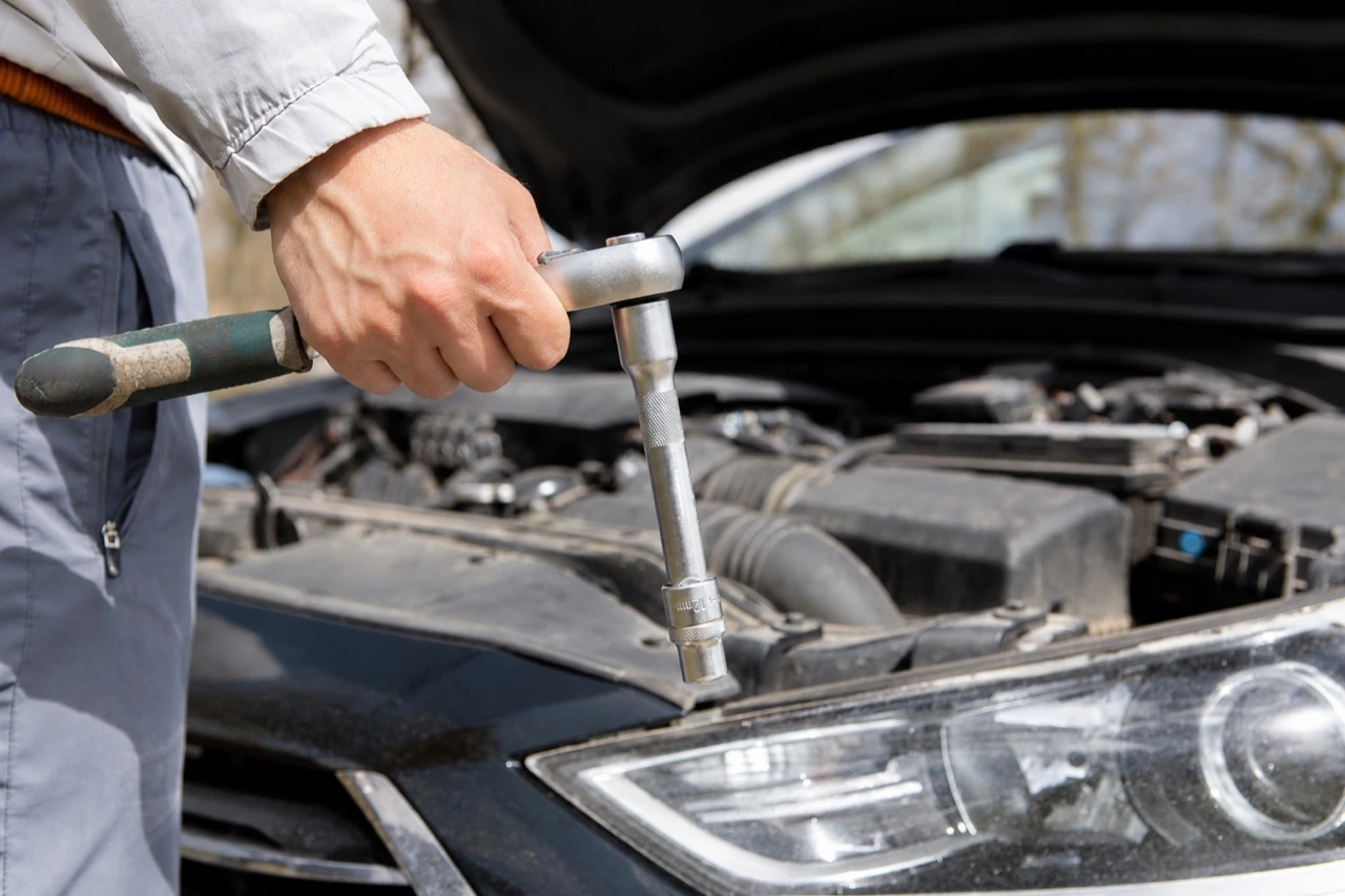 工具を手に自動車のエンジンルームを整備する様子