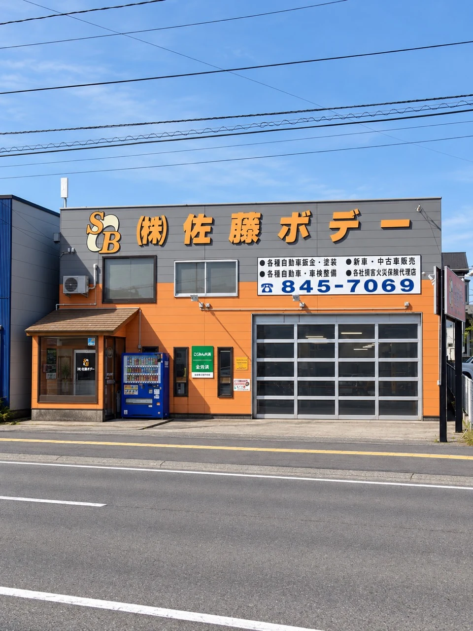 秋田市土崎の株式会社佐藤ボデー。オレンジとグレーの外観と、社名・電話番号が記された看板。